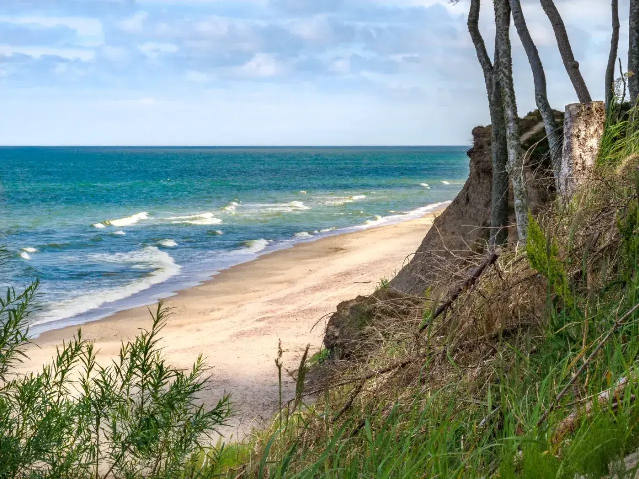 Spokojne miejsca nad morzem: piaszczysta plaża, turkusowe fale i klif porośnięty drzewami. Idealne na relaks.