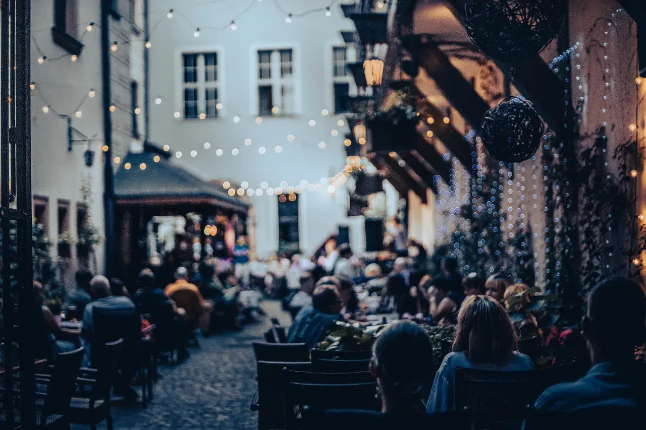 Wieczorny ogródek restauracyjny we Wrocławiu, pełen ludzi. Idealne miejsce na kolację, które z pewnością znajdzie się w rankingu restauracji Wrocław.
