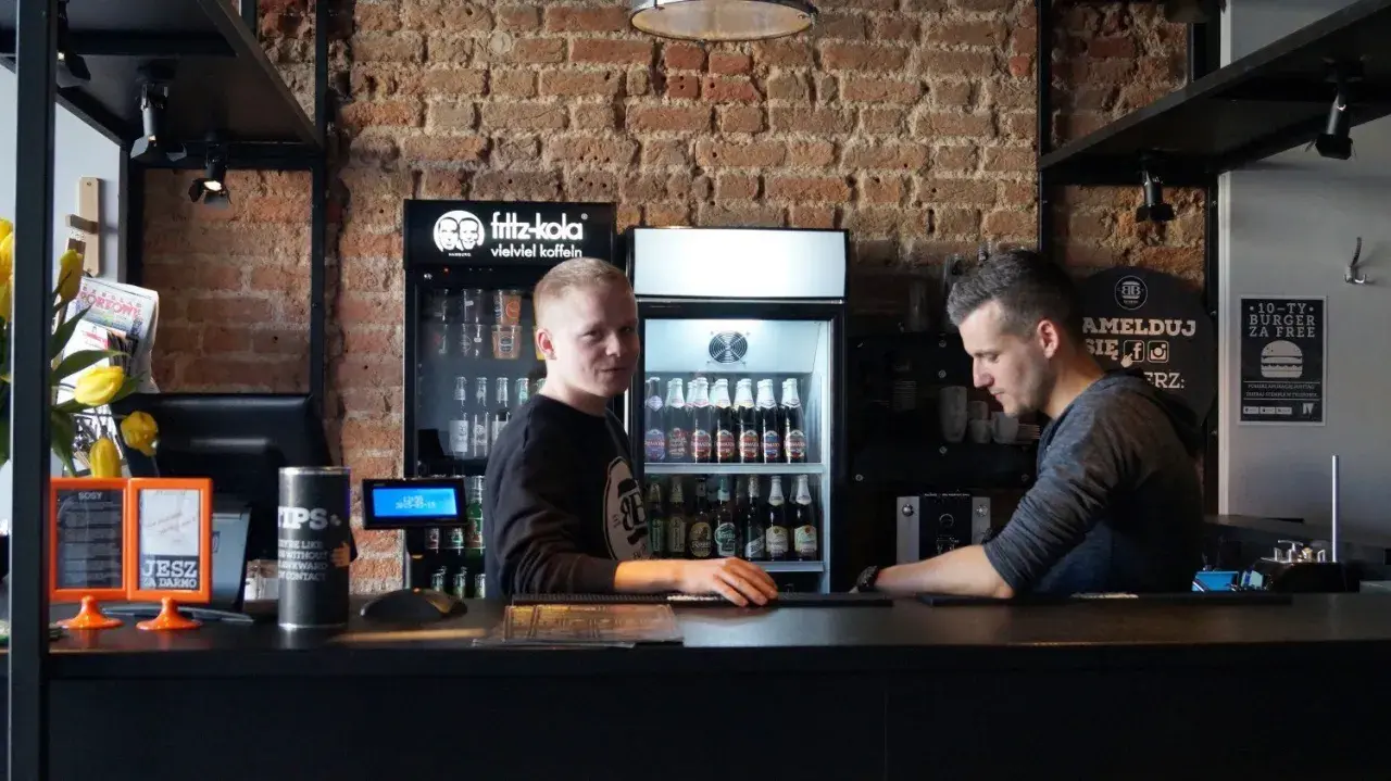 Pracownicy w Bobby Burger Bydgoszcz za ladą, obok lodówki z napojami i ekspresu do kawy.