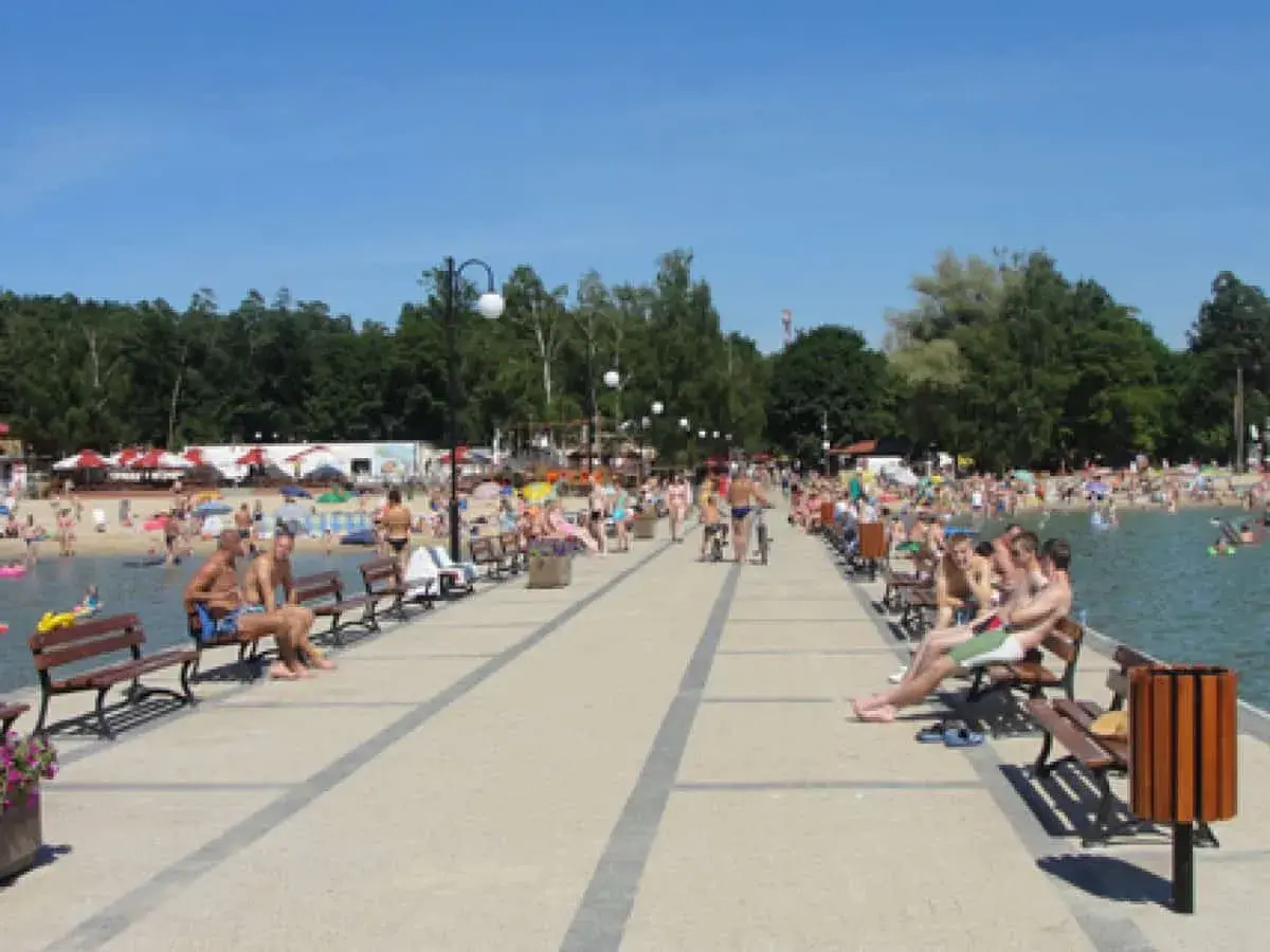 Ludzie odpoczywają na pomoście nad Skorzęcinem, jezioro tętni życiem, plaża pełna plażowiczów.