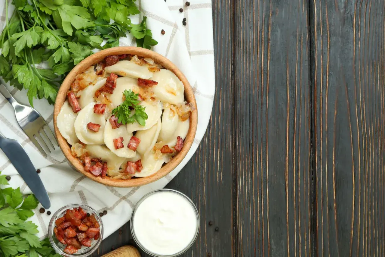 Pyszne pierogi z boczkiem i cebulką, serwowane w drewnianej misie. To kwintesencja kuchni łemkowskiej, podane z kwaśną śmietaną i świeżą natką pietruszki.