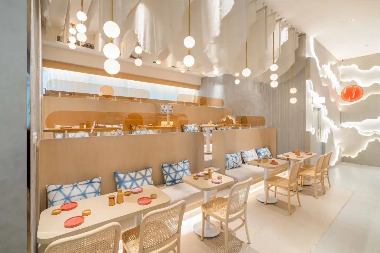 Nowoczesne wnętrze restauracji z drewnianymi elementami i białymi zasłonami. Stoliki z naczyniami do sushi. Idealne miejsce na ranking sushi Warszawa.
