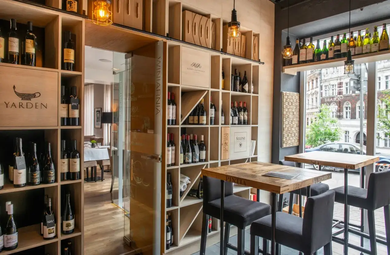 Wnętrze restauracji Muga z regałami pełnymi win. Drewniane stoły i krzesła tworzą przytulną atmosferę.