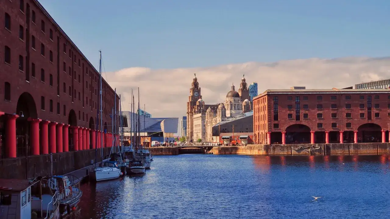 Widok na zabytkowe doki i charakterystyczne budynki w Liverpool miasto. Woda odbija niebo i chmury.