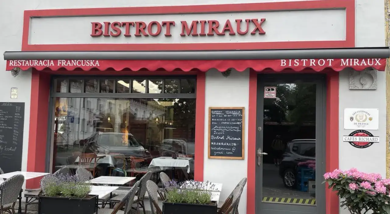 Elegancka restauracja francuska Bistrot Miraux z czerwonymi markizami i stolikami na zewnątrz.