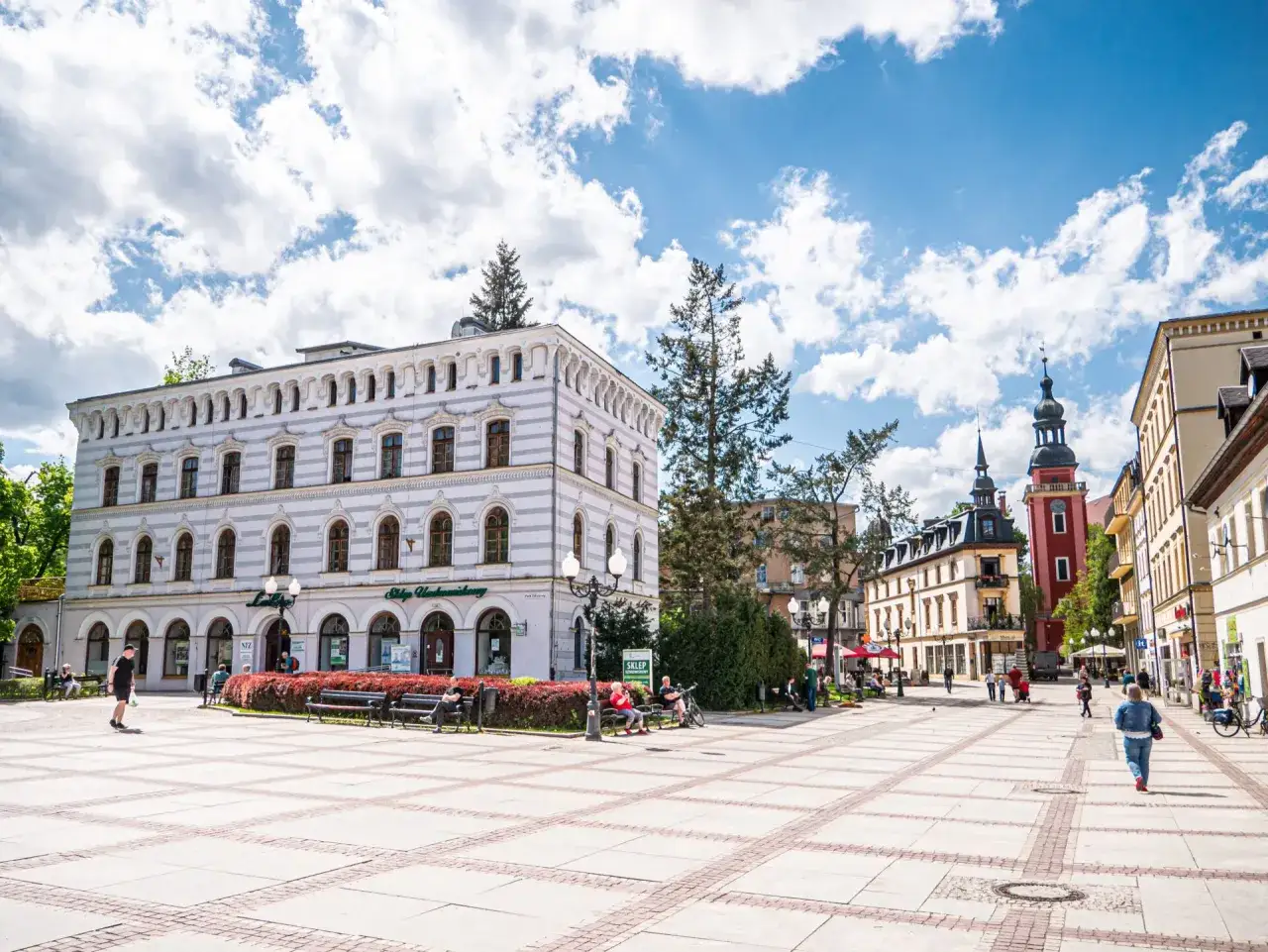 Rynek w Cieplicach tętni życiem. Ludzie spacerują, siedzą na ławkach, ciesząc się słońcem i architekturą.