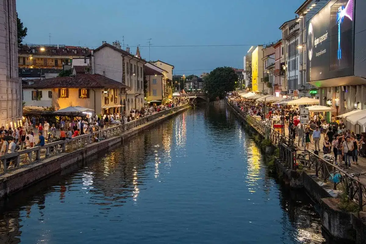 Tłum ludzi spaceruje wzdłuż kanału Navigli w Mediolanie, gdzie restauracje i bary tętnią życiem wieczorem.