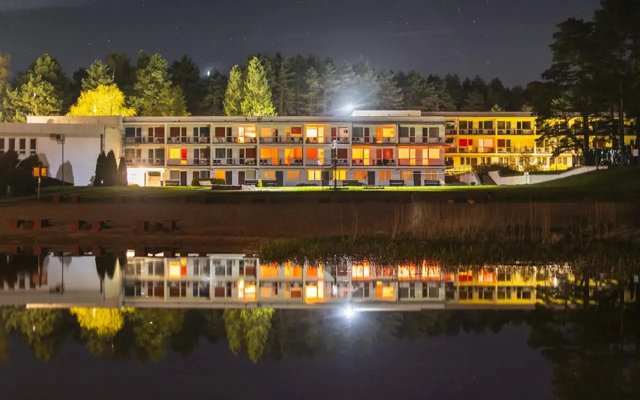 Nocny widok na hotel nad zalewem zemborzyckim. Oświetlone okna odbijają się w spokojnej tafli wody.