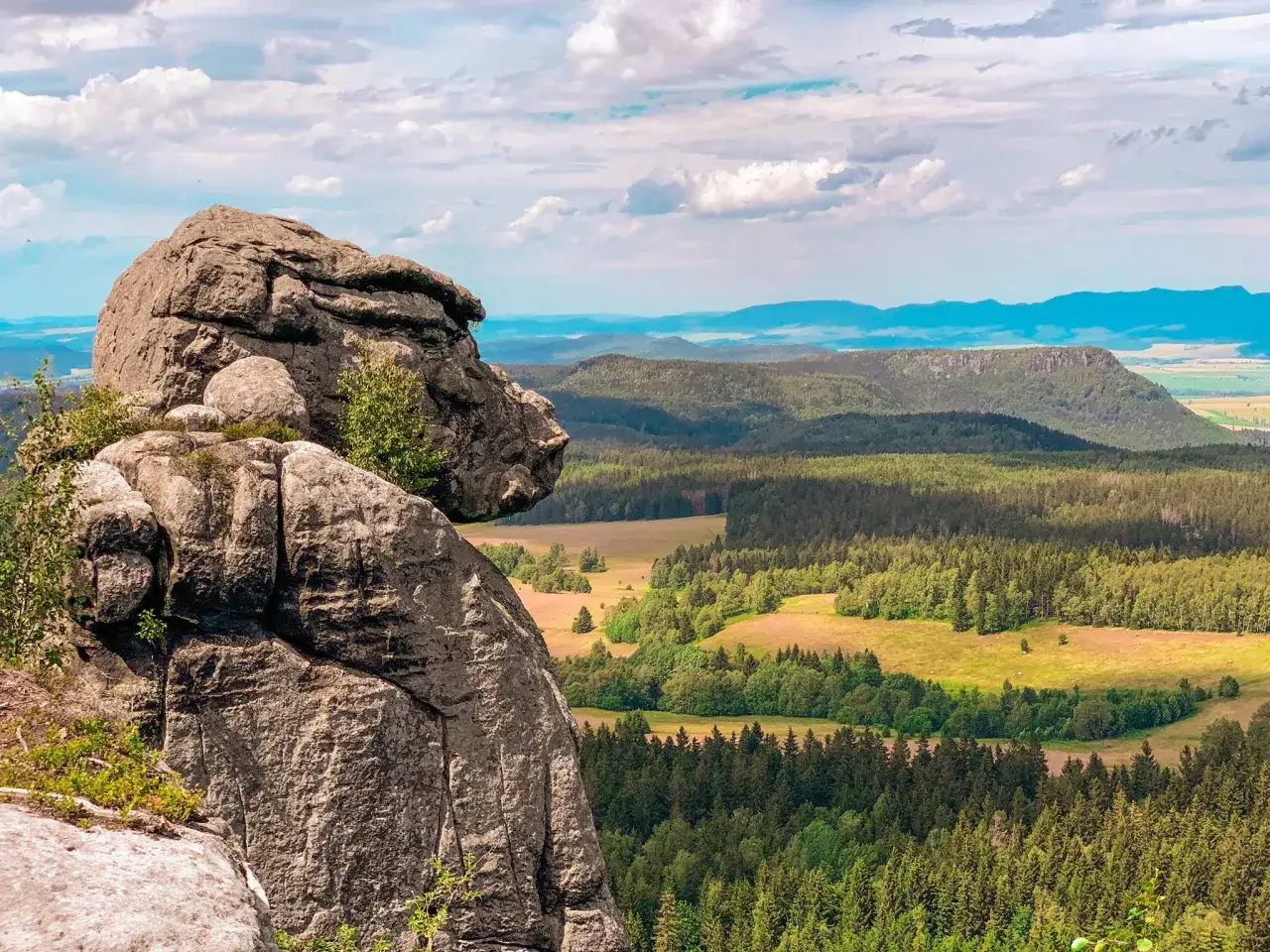 Skalny grzyb na pierwszym planie, a w oddali rozległe, zielone doliny i płaskie szczyty. Tak właśnie wyglądają Góry Stołowe.