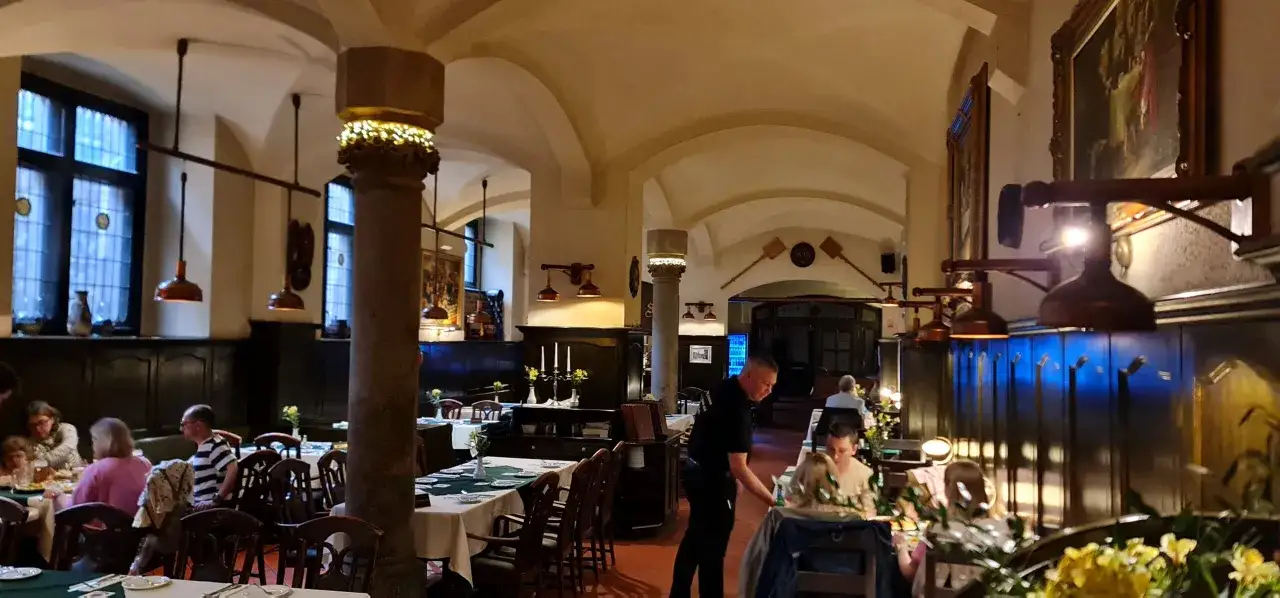 Wnętrze zabytkowej restauracji, gdzie serwuje się dania. Widać stoły z białymi obrusami, drewniane kolumny i obrazy. To może być najstarsza restauracja w Polsce.