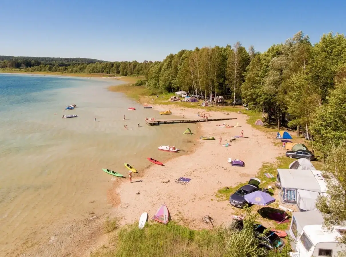 Wakacje nad jeziorem Świętajno: plaża, namioty, kajaki i ludzie kąpiący się w czystej wodzie.