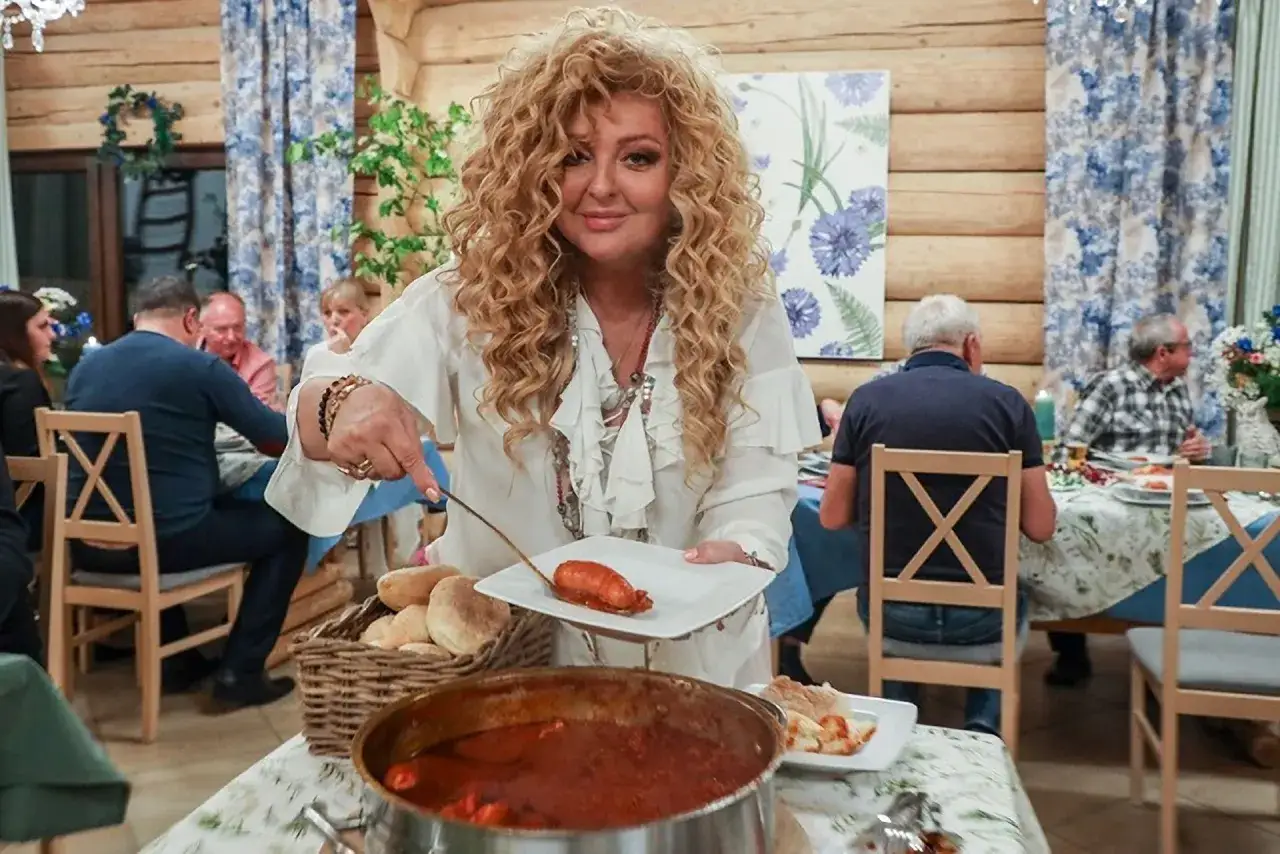 Magda Gessler serwuje barszcz w Wejherowie. W tle goście siedzą przy stole w drewnianej karczmie.