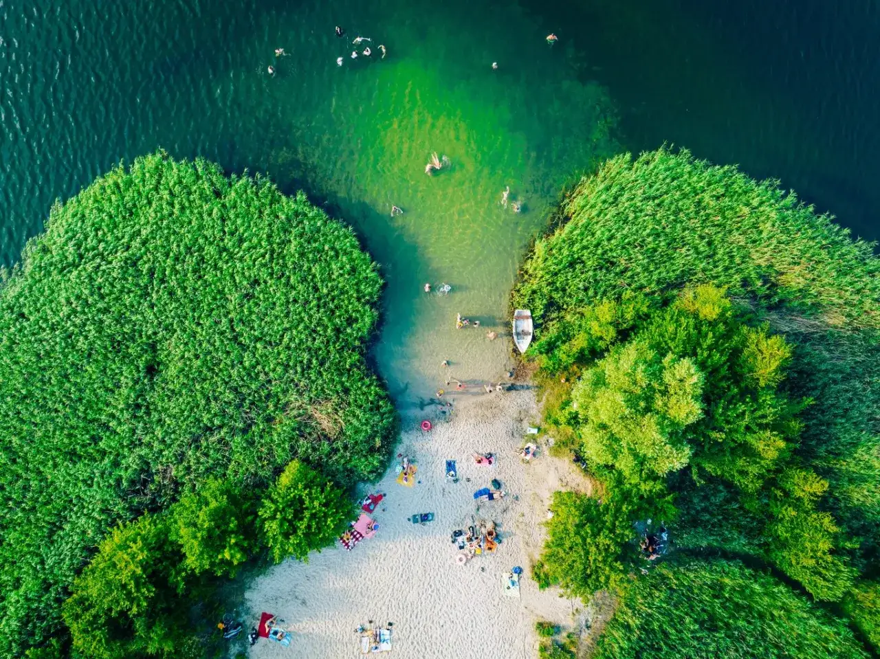 Letnie popołudnie nad jednymi z malowniczych jezior na południu Polski. Ludzie kąpią się, opalają na plaży, a łódka czeka przy brzegu.