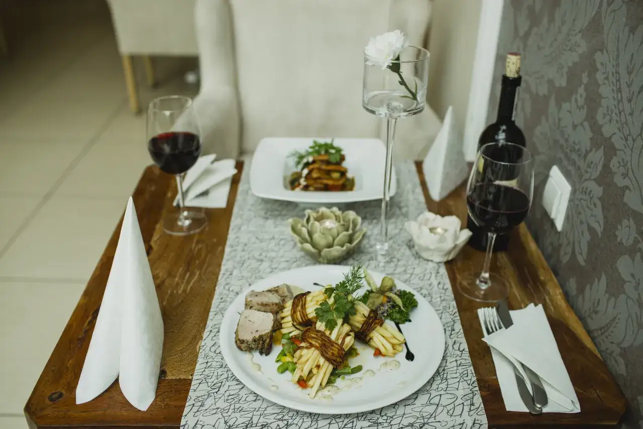 Elegancka kolacja we dwoje w Opolu. Dwa talerze z wykwintnymi daniami, kieliszki z czerwonym winem i świece tworzą romantyczny nastrój. Idealne opole atrakcje dla par.