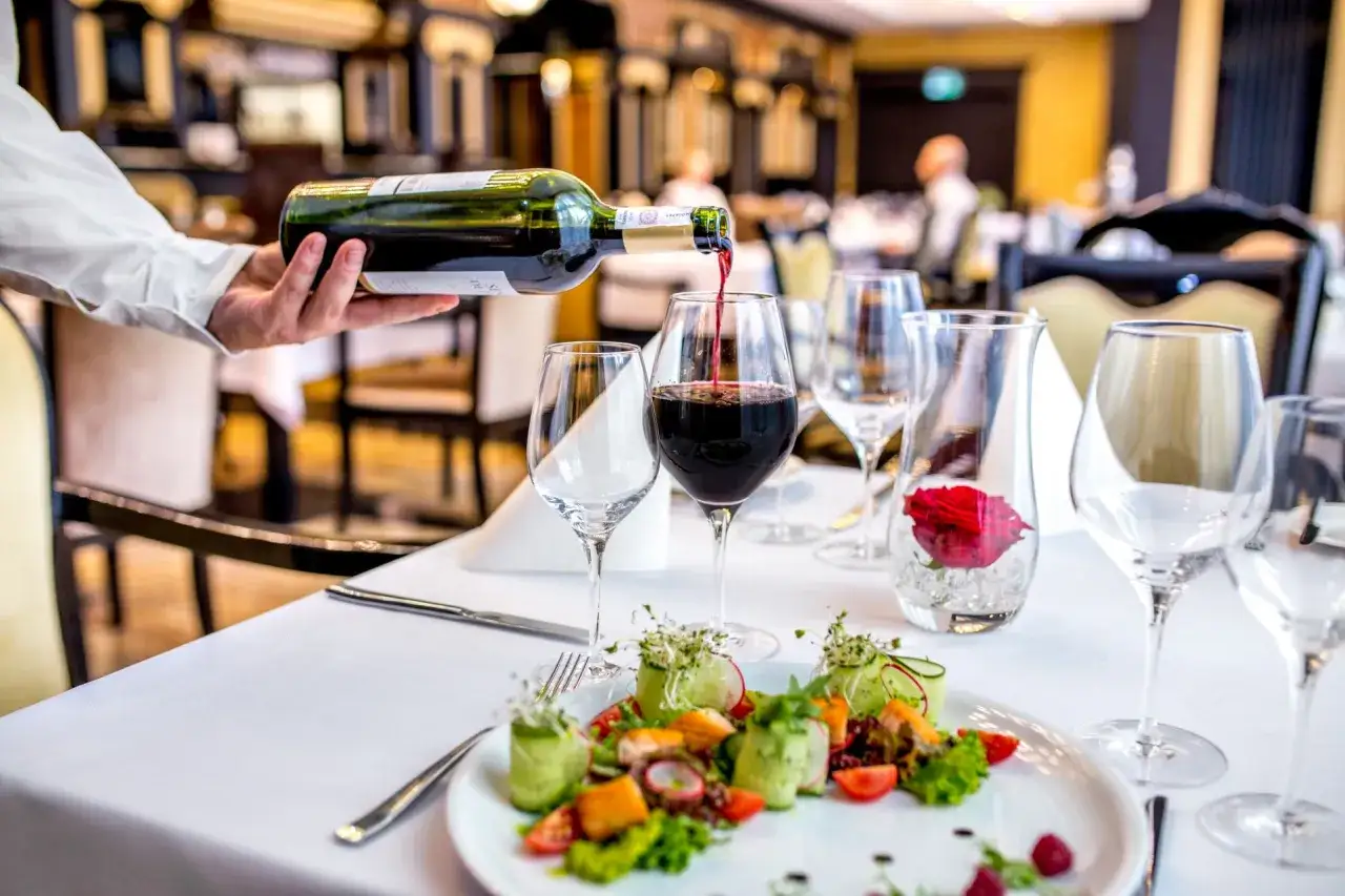 Elegancka kolacja w jednej z najlepszych restauracji Szczecin ranking. Kelner nalewa wino do kieliszka, obok danie z rybą i warzywami.