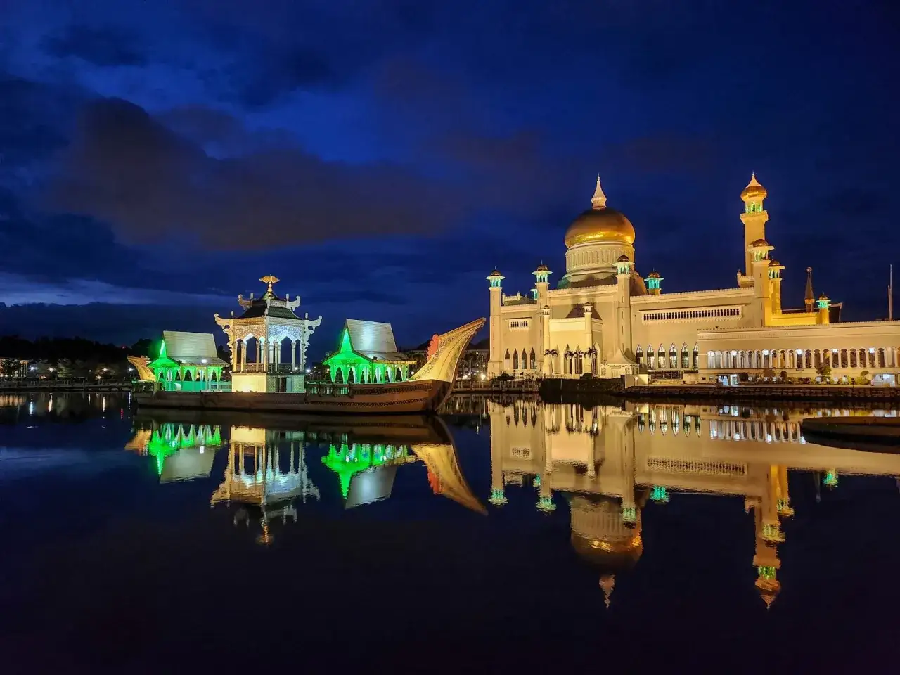 Wspaniała nocna panorama wyspy z Brunei. Złota kopuła meczetu i zielono oświetlona łódź odbijają się w spokojnej wodzie.