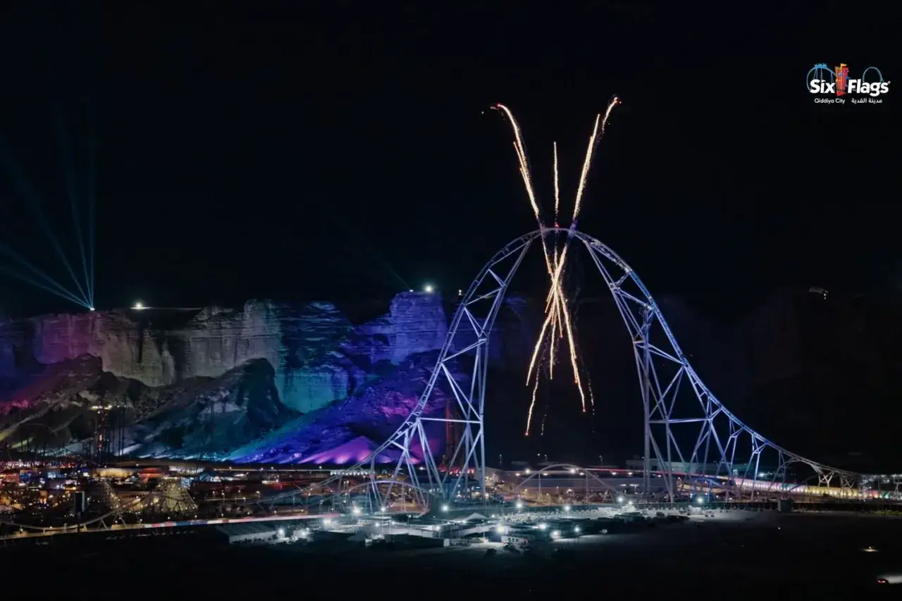 Nocna iluminacja najwyższego rollercoastera na świecie w Qiddiya City. Fajerwerki rozświetlają niebo nad imponującą konstrukcją.