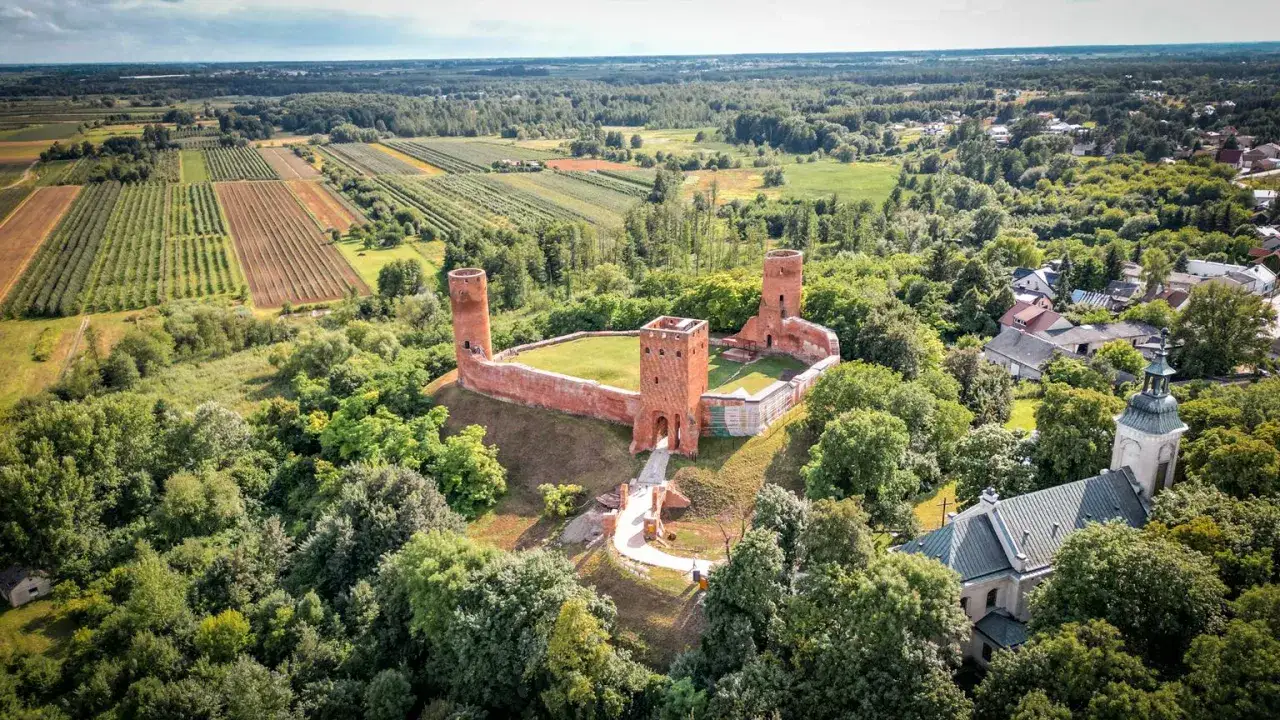 Ruiny zamku w krajobrazie rolniczym, otoczone lasem. W oddali widać pola uprawne i zabudowania. To widok z największego województwa w Polsce.