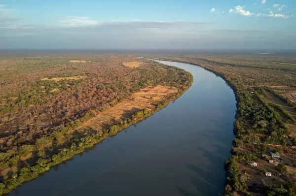 Szeroka rzeka Niger meandruje przez sawannę, otoczona bujną roślinnością i nielicznymi osadami.