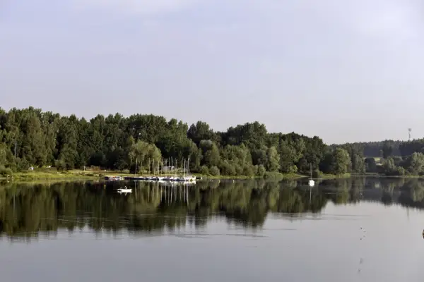 Zalew Przeczyce z łodziami przy brzegu i samotną białą żaglówką na spokojnej tafli wody.